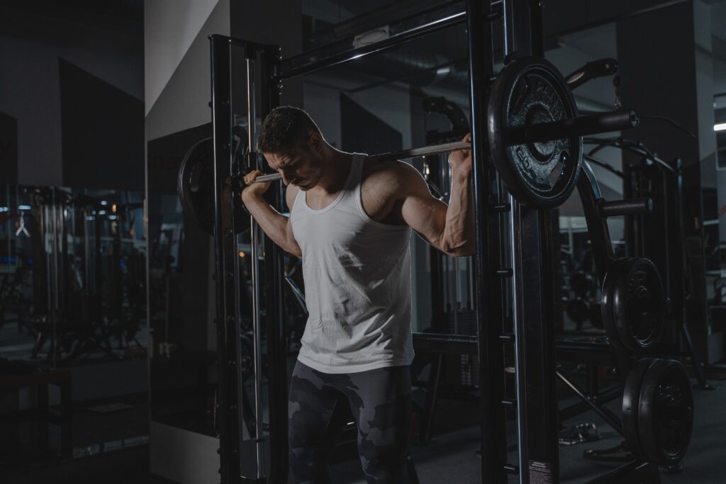 man in white tank top with barbell behind back